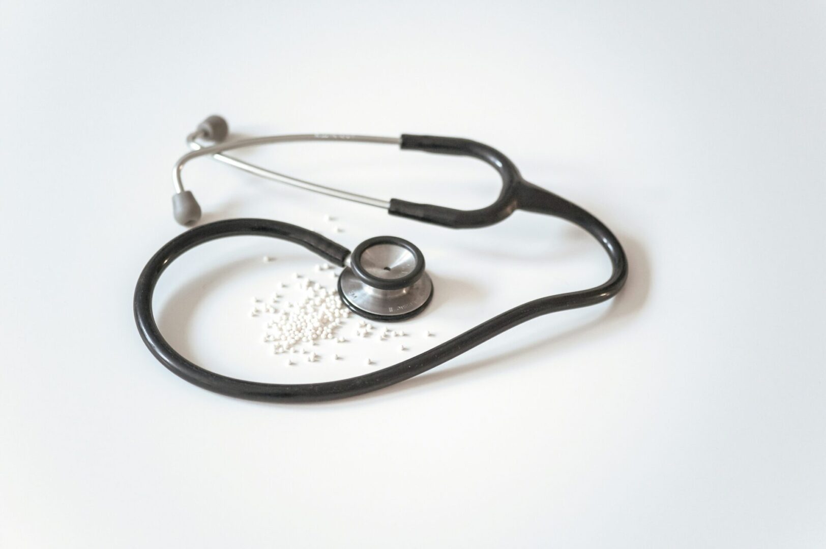 A stethoscope and scattered white pills on a white surface.